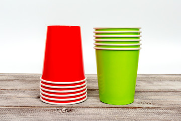 Two stacks of green and red take away disposable paper cups on wooden desk with white background