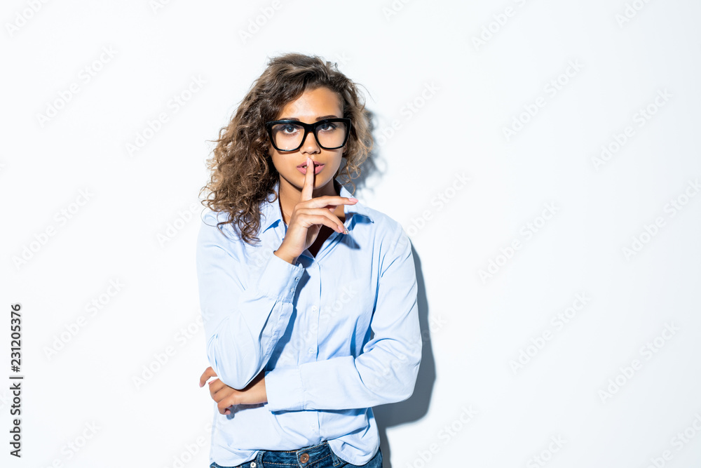 Wall mural shhh. curly pretty latin business woman in glasses making silence sign isolated on white background