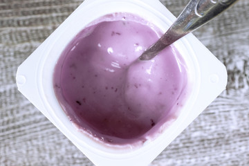 Blueberry yogurt in a plastic cup with a spoon inside on wooden background closeup