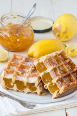 Sweet dessert. Homemade waffles with filling, fresh lemons and a small glass jar with fruit jam on an old wooden table.