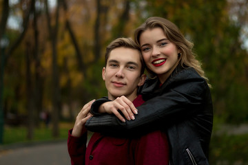 girl in a black jacket, smiling, hugging a guy. couple in love in the autumn park. family on vacation, date, lovers. hug from the back, come from the back.