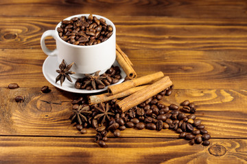 Coffee beans in white cup, cinnamon sticks and star anise on wooden table