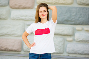 Naklejka na ściany i meble Portrait of a beautiful girl in casual white t-shirt on the brick wall background touching her hair