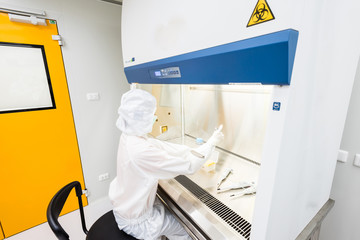 A scientist in sterile coverall gown pipetting medium or reagents for cell culture experiment in...
