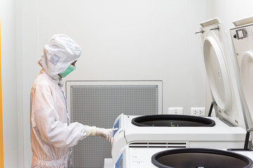 A scientist in sterile coverall gown using laboratory equipment (refrigerated centrifuge) for doing...