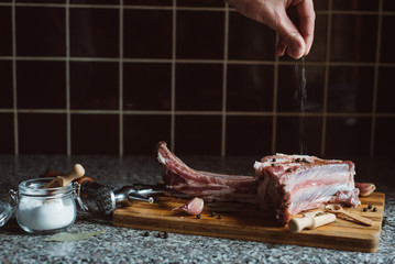 cook adds spices on raw meat on wooden cutting board
