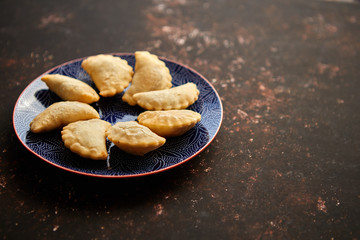 Hot and tasty deep fried polish dumplings with meat filling placed on a blue ceramic plate. Top view on rusty brown background with copy space