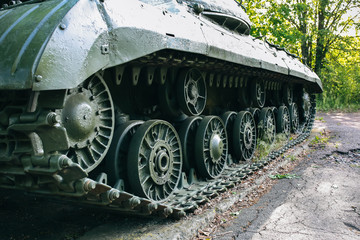 Old tank from the Second World war standing outdoors in the green forest. Caterpillar track of the armored fighting vehicle as a memory monument in peaceful times. No war concept.