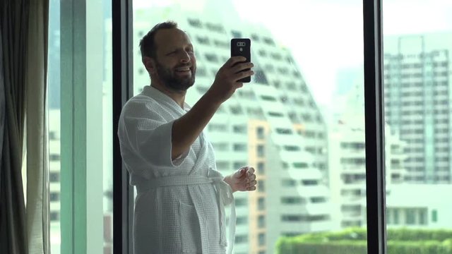 Happy man wearing bathrobe and doing selfies on smartphone, slow motion shot at 240fps