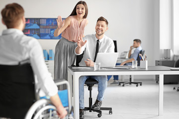 Young man in wheelchair with colleagues at workplace