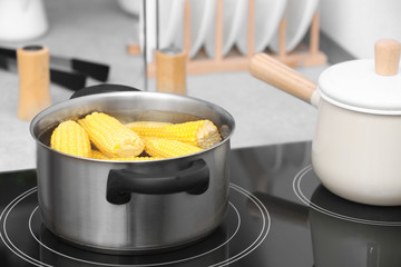 Stewpot with water and corn cobs on stove in kitchen