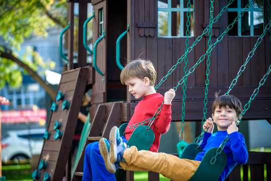 Smiling little boy and his brother friend on a swing. Children playing outdoors in summer. Healthy childhood friendship concept