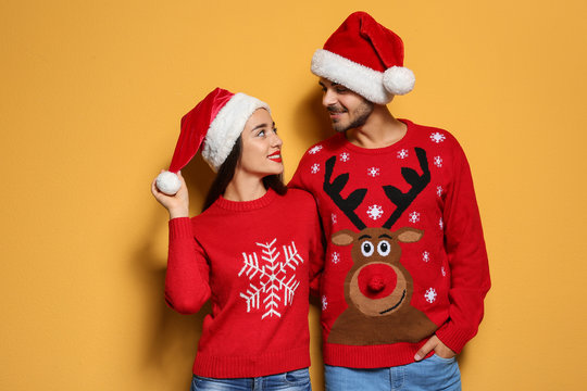 Young couple in Christmas sweaters and hats on color background