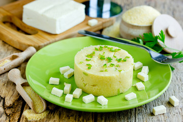 Polenta porridge with salty cheese on wooden table with ingredients
