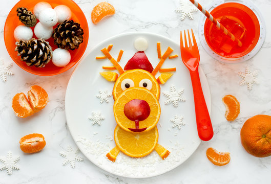 Fun Christmas food art idea - edible reindeer from orange slices on white plate, healthy fruit snack for kids