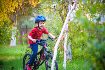 Happy kid boy of 6 years having fun in autumn forest with a bicycle on beautiful fall day. Active child making sports. Safety, sports, leisure with kids concept