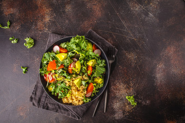 Avocado, quinoa, yam and kale salad in black plate on a dark background.