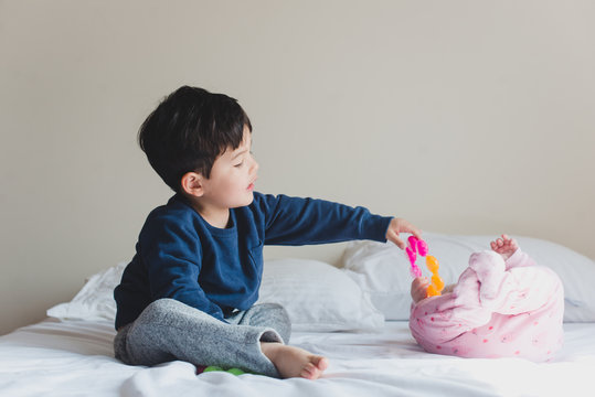 Toddler boy sharing toy with baby sister