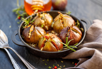 Baked figs stuffed with gorgonzola cheese, pine nuts, honey and herbs in a black dish on a dark,...