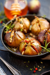 Fototapeta na wymiar Baked figs stuffed with gorgonzola cheese, pine nuts, honey and herbs in a black dish on a dark, stone background, close up. Excellent, tasty, vegetarian snack, appetizer