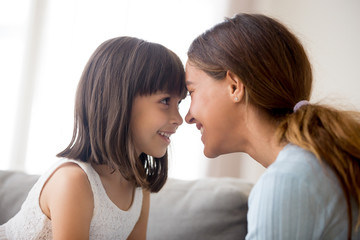 Close up beautiful happy mother and daughter touching with foreheads looking at each other with love tender and devotion, mom expressing support understanding candid emotions sitting on couch at home