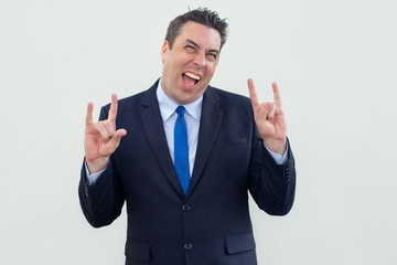 Jolly cool businessman showing signs of horns and having fun. Cheerful middle-aged man in suit gesturing hands and screaming in excitement. Cool man concept