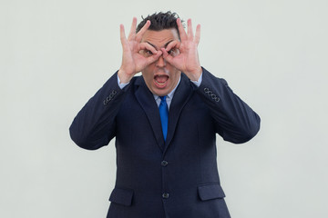 Surprised intelligent businessman looking through finger glasses. Cheerful shocked man in formal suit opening mouth. Curiosity concept