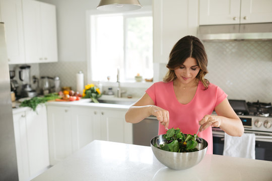 Woman making and tossing salad at home