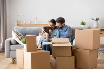 Diverse family parents and little daughter sitting together on sofa in living room at new home....