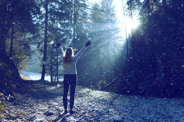 Woman raises her hands and breathing cold air during a sunny winter morning during snowfall....