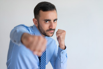 Aggressive young bearded businessman punching camera. Serious handsome man boxing against white background. Challenge concept