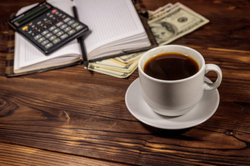 Cup of coffee and notepad with dollars, pencil and calculator on wooden desk. Financial concept