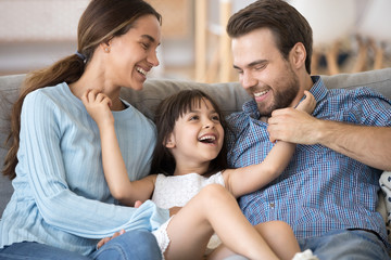 Close up smiling cheerful daughter tickling parents people have fun playtime together at home....