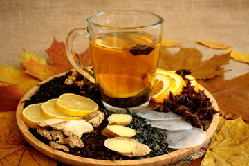 Rozgrzewająca jesienna herbata, różne rodzaje herbaty i przyprawy na tacy, obok jesienne liście - obrazy, fototapety, plakaty