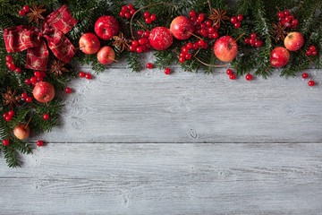 Christmas wooden background with fir branches, red apples and berries