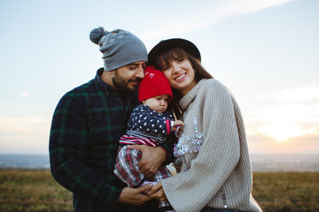 Parents hold their little girl in their arms. Photo session with family at sunset.
