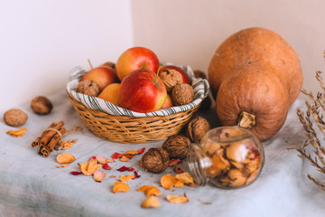 Still life with cinnamon sticks wrapped in twine, pumpkin, apples in a wicker basket stand on a striped linen cloth, walnuts and flower petals in bank. Concept of home comfort in autumn or winter. 