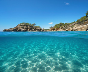 Fototapeta premium Rocky coast with an islet and sand underwater, split view half above and below water surface, Mediterranean sea, Catalonia, l'Illot, L'Ametlla de Mar, Tarragona, Costa Dorada, Spain