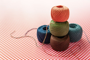 Multicolored spools of cotton thread on a red checkered background. Selective focus, space for text.