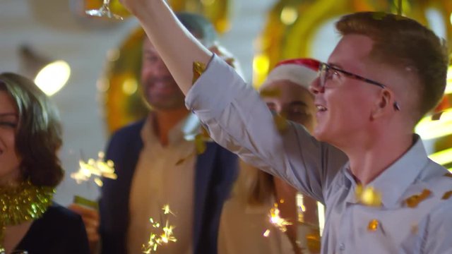 Handheld tracking shot of happy people holding glasses of champagne and sparklers laughing and dancing at Christmas party