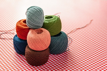 Multicolored spools of cotton thread on a red checkered background. Selective focus, space for text.