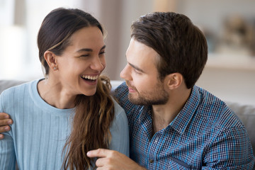 Head shot portrait cheerful diverse married couple in love sitting in living room on couch. Young husband embrace wife talking laughing spending time having good mood enjoying time at home together