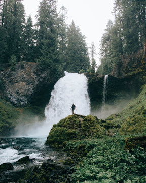 Person standing on a rock in front of a waterfall