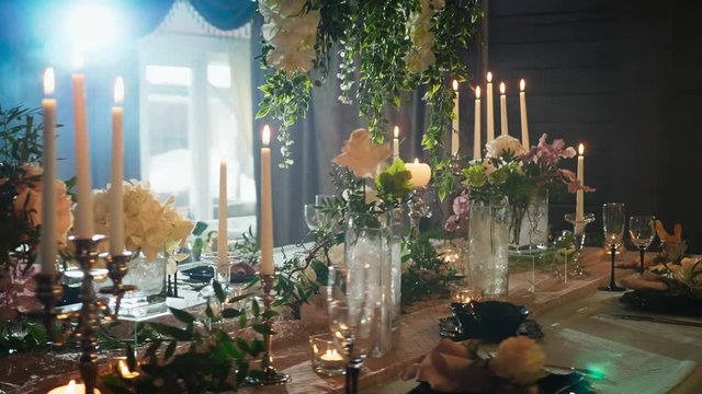 a row of wine glasses and candle holders on a table served with black plates, candlesticks with candles and flower vases