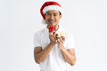 Smiling man wearing Santa hat and showing small gift boxes. Asian guy looking at camera. Christmas gifts concept. Isolated front view on white background.