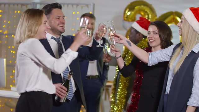 PAN shot of happy businessman and laughing businesswomen clinking glasses and dancing at office Christmas party