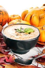 Roasted pumpkin and carrot soup with cream and pumpkin seeds on wooden background.