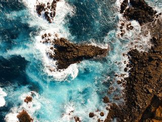 Obraz premium Aerial top view of sea waves hitting black volcanic rocks on the coastline with turquoise sea water. Amazing rock cliff seascape in the Portuguese coastline. Azores islands. Drone shot.