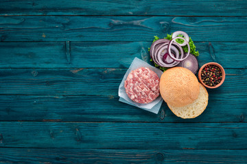 Preparation of burger. Meat, tomatoes, onions. On a blue wooden background. Top view. Free copy space.