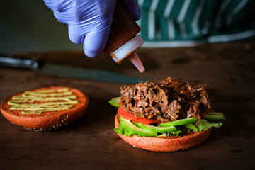 process of making burger. chef hands in gloves cooking beefburger with avocado and tomato